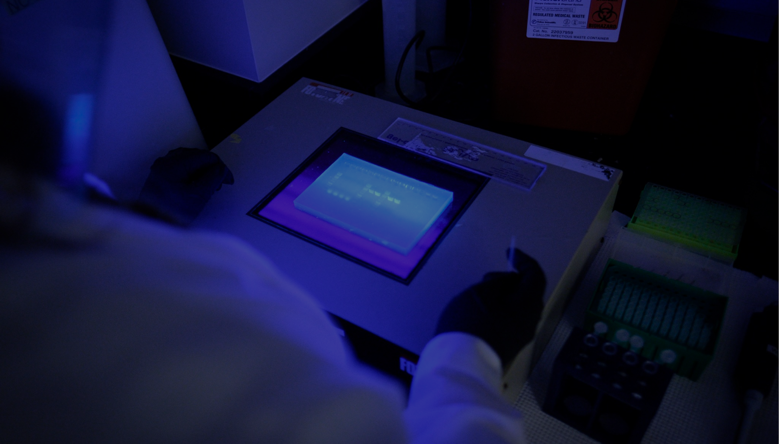 A lab technician works with equipment in a darkly lit room.